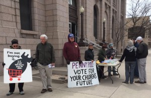 people with signs: “I'm not buying it”, “Penny Poll: Vote for your children's future”